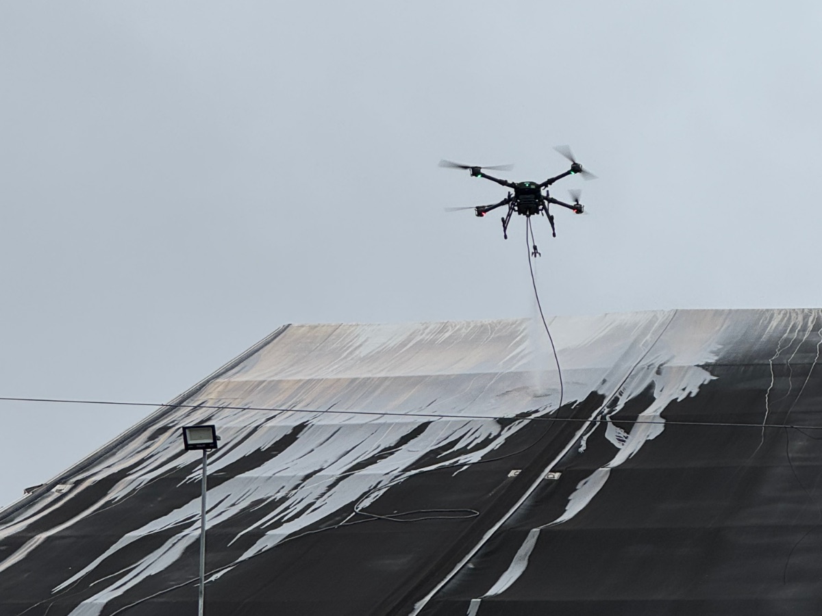 Drone lavando cobertura de lona escura, com faixas já limpas à mostra