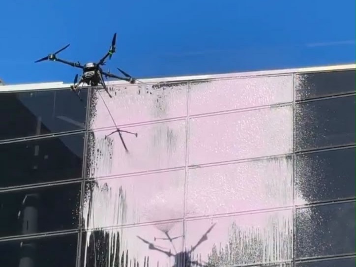 Drone lavando fachada de vidro, com espuma sobre os painéis